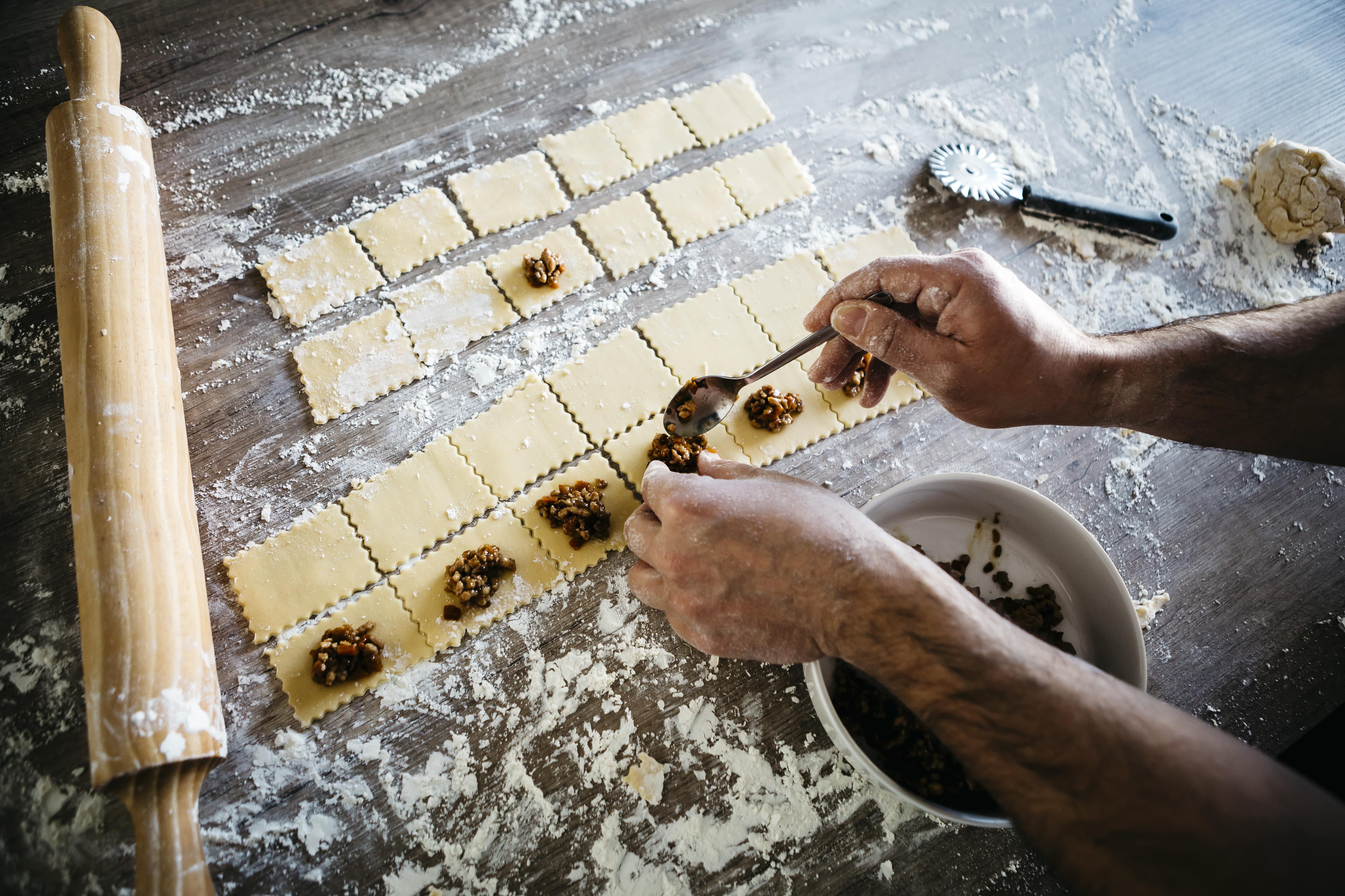 sfeerbeeld close-up van het maken van verse ravioli, twee handen bekleden een helft van de ravioli met vers vlees.