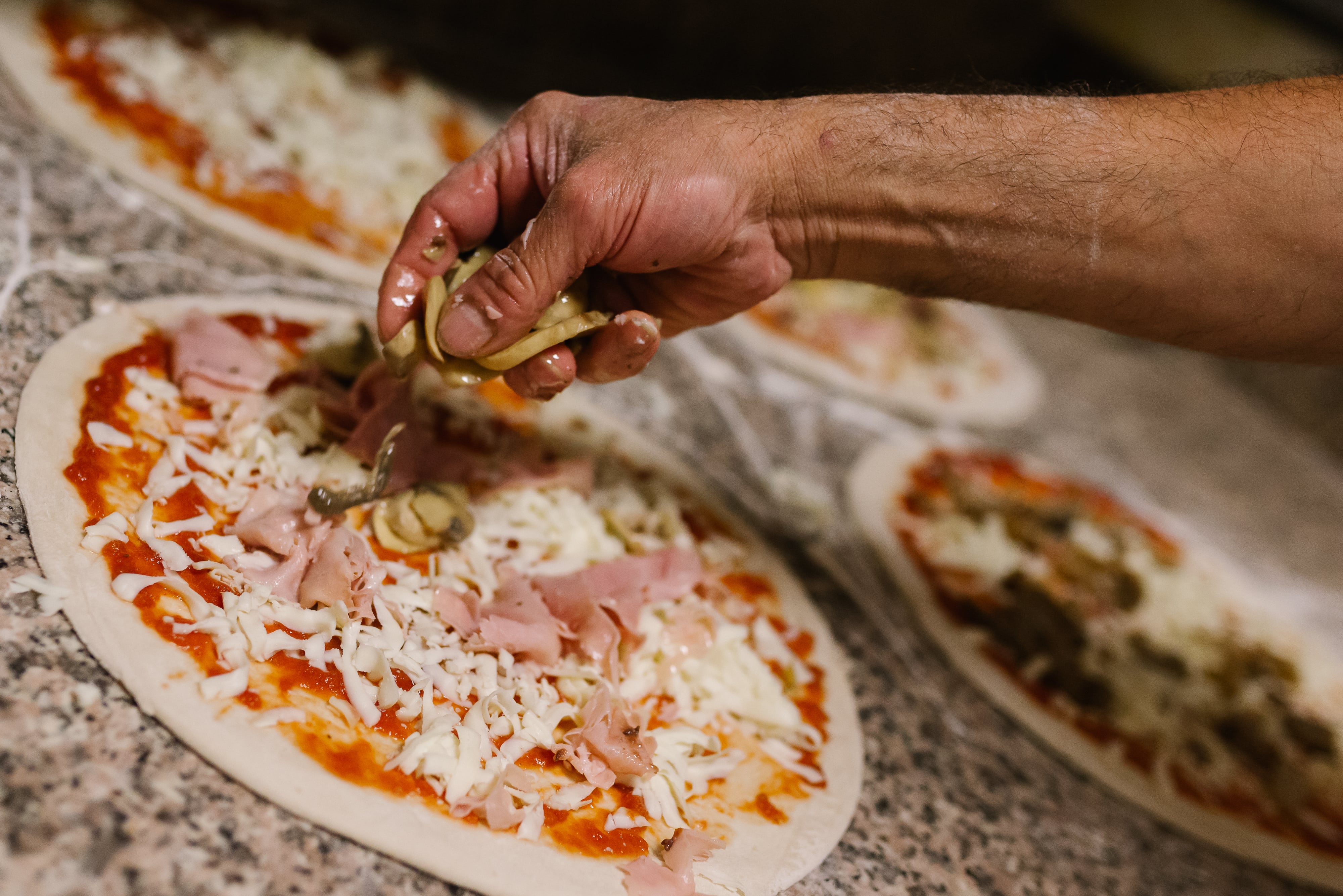 Sfeerbeeld pizza maken in close-up, een hand strooi verse champignons op een rijkelijk belegde pizza klaar voor in de oven.