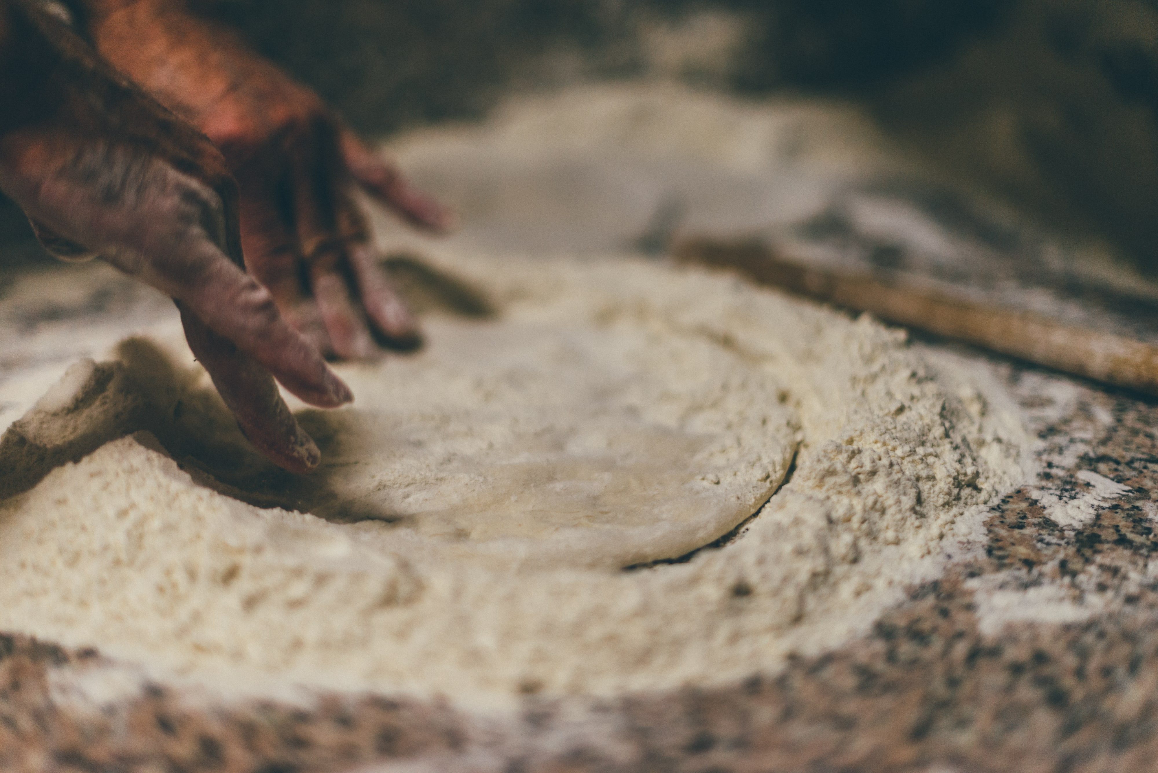 Sfeerbeeld in close-up pizza maken, twee handen duwen met de vingertoppen het ronde met bloem bestrooid deeg platter